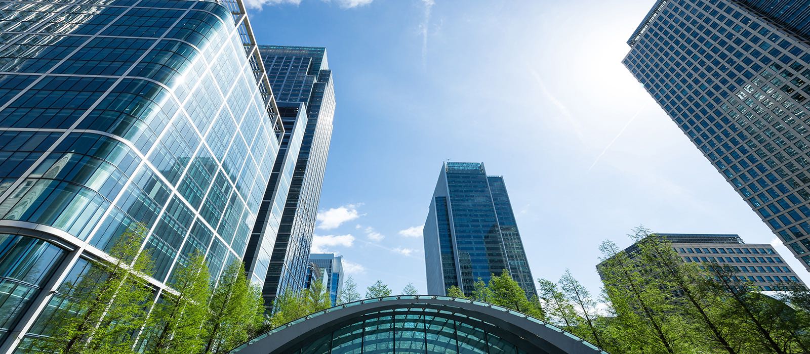 View of modern skyscrapers under a clear blue sky with sunlight streaming down.